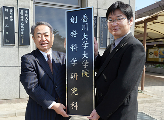 新研究科の看板を掲げ記念撮影を行う筧学長（左）と末永研究科長（右）